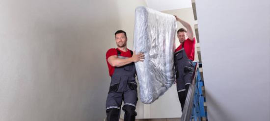 junk removal workers carrying mattress down stairwell